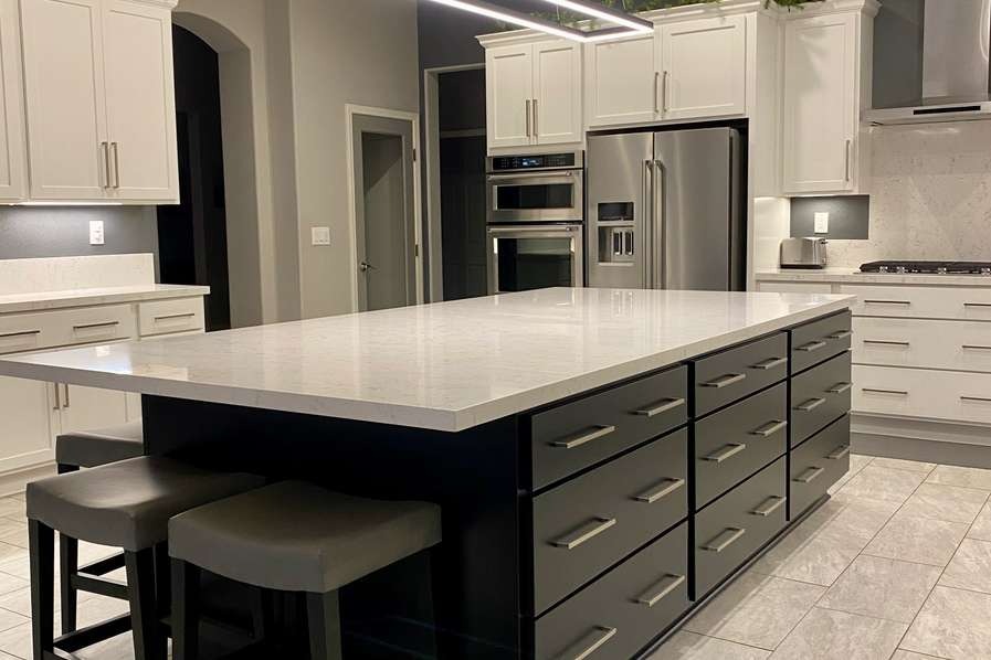 Oversized black island with waterfall quartz top, drawer bank and white perimeter cabinets