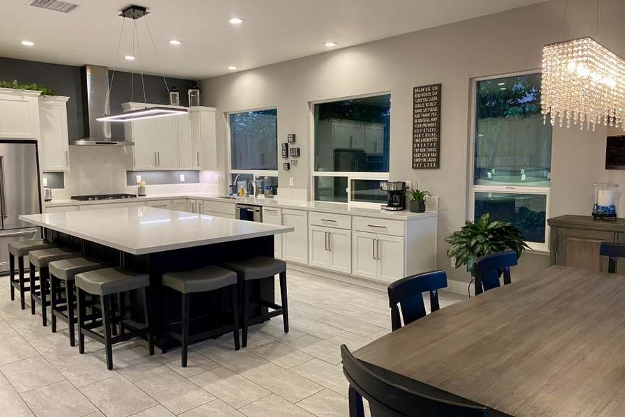 Great-room kitchen with a long seating island, white shaker cabinets and linear pendant