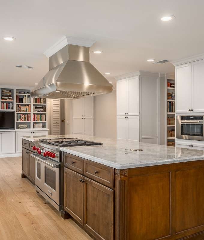 Yancey-built kitchen with a stained wood island, marble counters, pro range and stainless chimney hood
