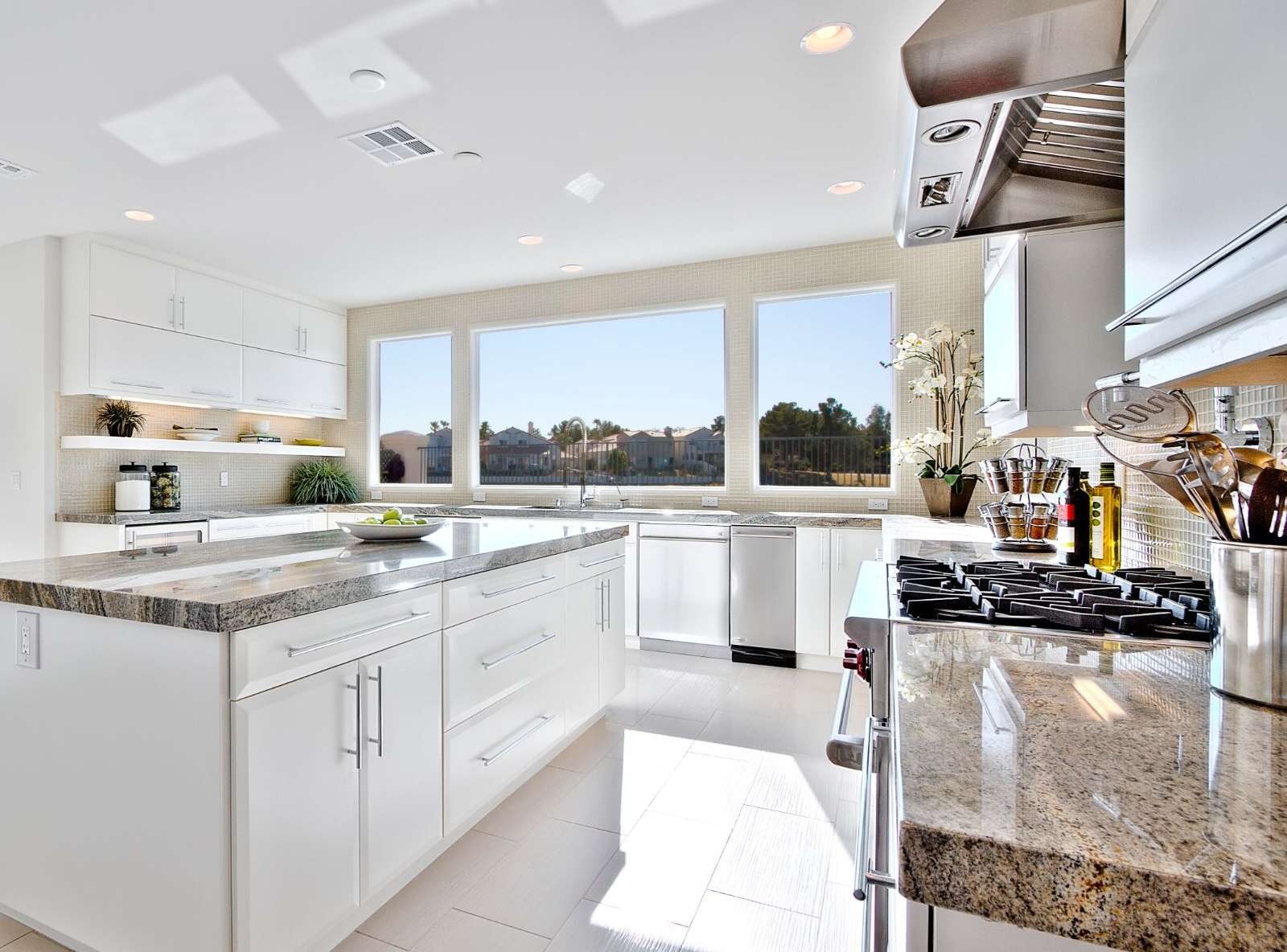 Modern white kitchen with granite island, glass mosaic backsplash and stainless pro hood