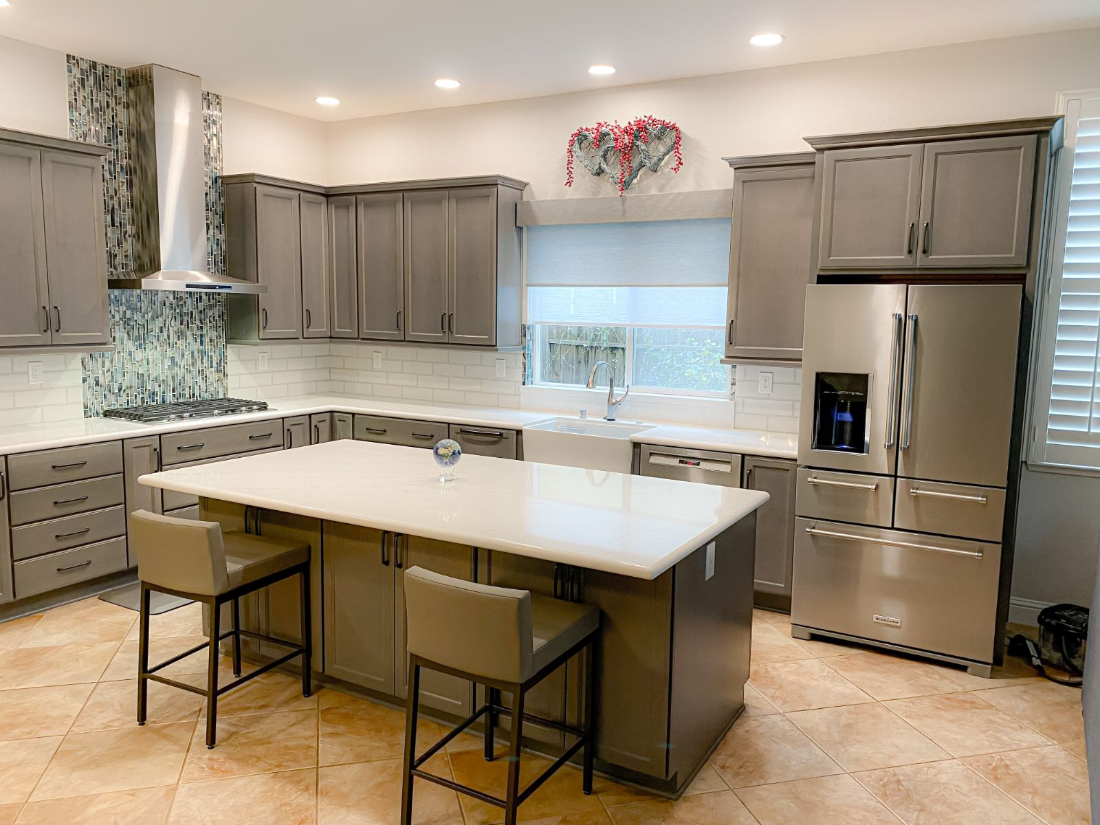 Remodeled gray kitchen with quartz island, farmhouse sink and glass mosaic hood surround