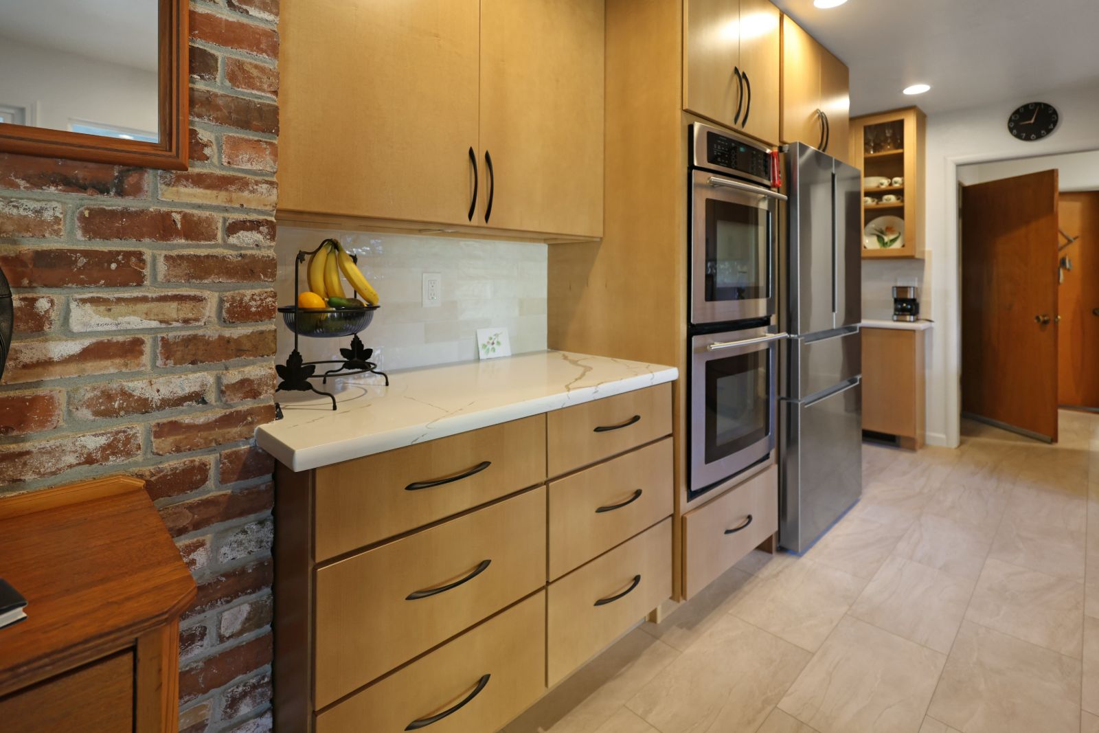Maple slab cabinets with quartz counters, double wall ovens and an exposed brick wall